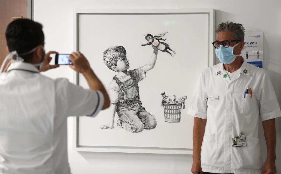 Ein medizinischer Mitarbeiter lässt sich vor dem Banksy-Werk "Game Changer" fotografieren