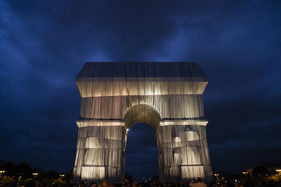 Eine Nachtaufnahme zeigt den Arc de Triomphe in Paris, der nach dem Entwurf des verstorbenen Künstlerpaars Christo und Jeanne-Claude in silberblauen Stoff gehüllt wurde