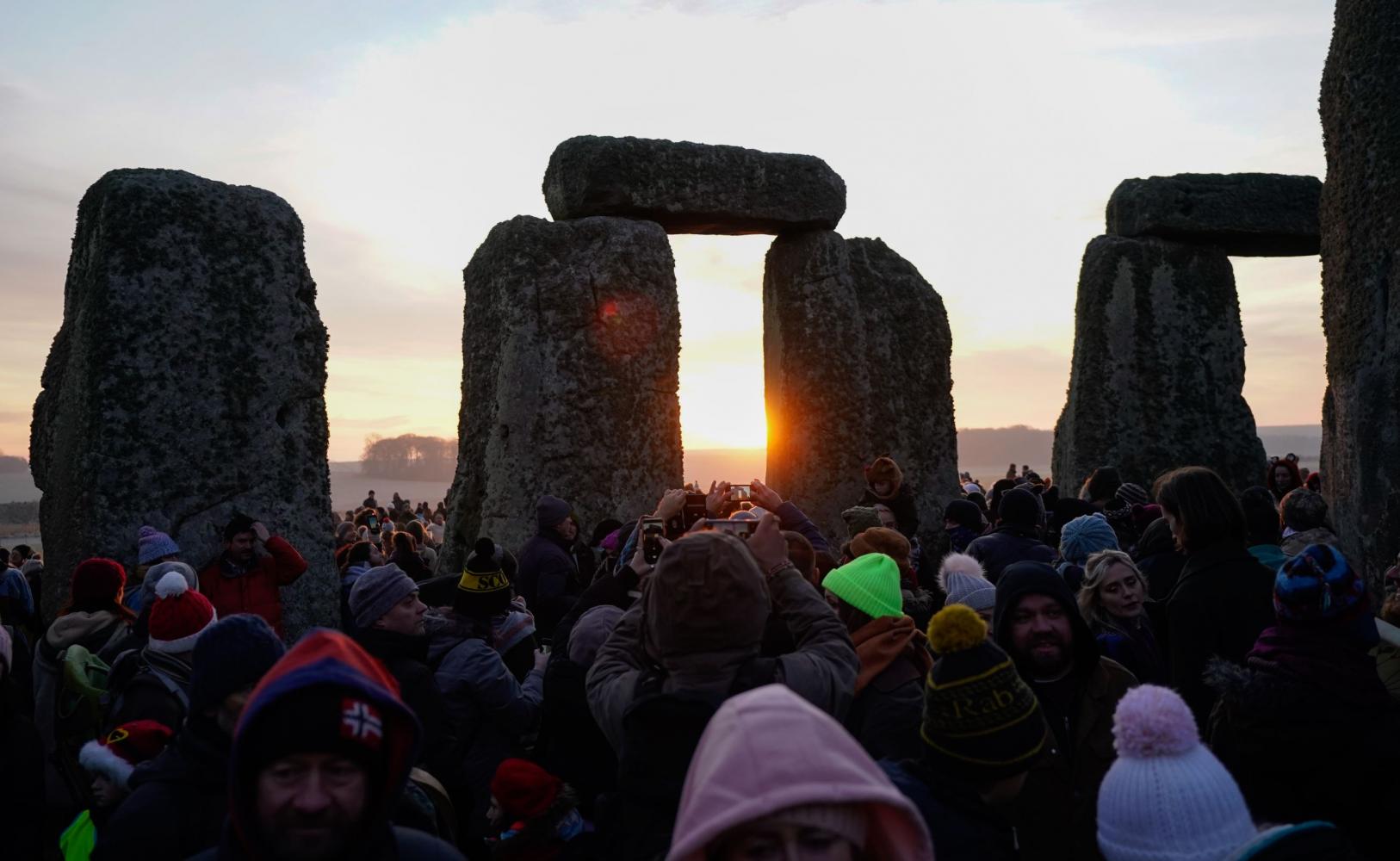  Die Sonne geht hinter de prähistorischen Monument von Stonehenge auf, während Menschen versammeln, auf der Salisbury Plain die Wintersonnenwende feiern